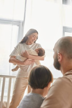Yeni doğmuş bebeğini bulanık koca ve küçük oğlunun yanında tutan güzel anneye odaklan.