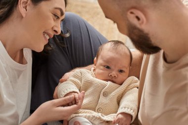 Neşeli modern ebeveynler yeni doğmuş bebekleriyle vakit geçiriyorlar ve ona gülümsüyorlar, aile kavramı.