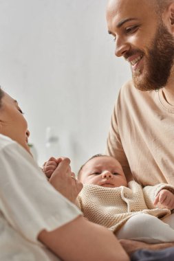 Yeni doğmuş erkek bebeklerini kucağında tutan ev elbiseli mutlu ebeveynlerin dikey çekimi. Aile kavramı.