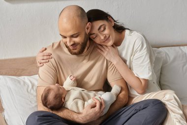 Samimi ev kıyafetleri içinde mutlu ebeveynler yeni doğmuş bebeklerini kucaklıyor ve kucaklıyorlar, aile kavramı