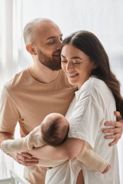 vertical shot of jolly happy parents hugging lovingly and holding their newborn baby boy, family clipart