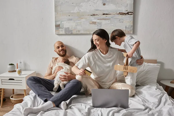 快乐而美丽的家庭与笔记本电脑 信用卡 现代的育儿方式在床上共度时光 — 图库照片