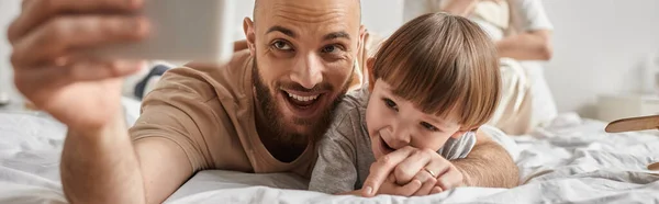 stock image joyous bearded father taking selfies with his little son while lying on bed, family concept, banner