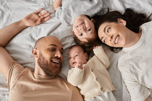 top view of cheerful beautiful family spending time together lying in bed, modern parenting