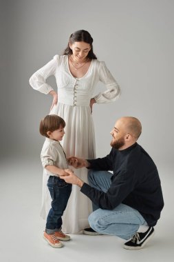 Dikey çekimde, mutlu anne ayakta durup kocasına bakıyor. Oğluna, ailesine çömelmiş.