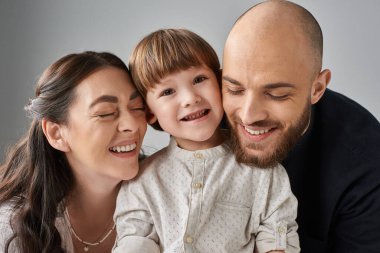 Neşeli, sevgi dolu ebeveynler, kapalı gözlerle gülümsüyorlar. Neşeli küçük oğullarına sarılıyorlar, aile kavramına.