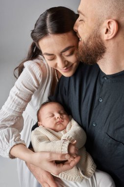 vertical shot of loving mother looking at her baby boy while her husband kissing her forehead clipart