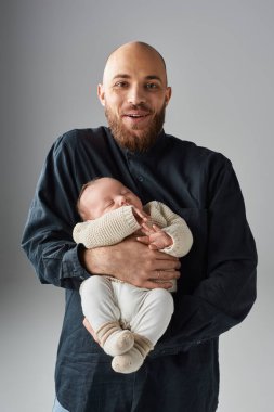 Yakışıklı, neşeli baba yeni doğmuş bebeğini kucağında tutuyor ve mutlu bir şekilde kameraya gülümsüyor.