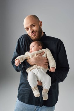 Bebeğini kucağında tutan sakallı yakışıklı adamın dikey görüntüsü ve kamera, aile kavramı.