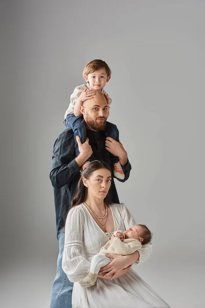 stock image jolly mother sitting and holding newborn baby with her husband holding their little son on shoulders