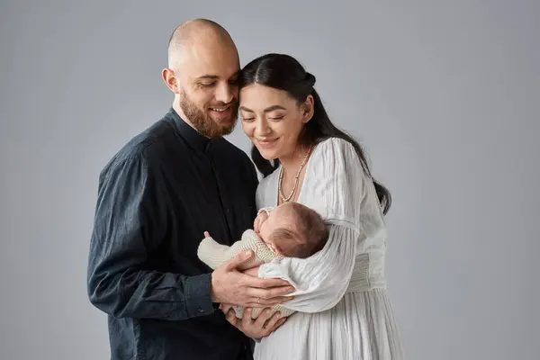 灰色の背景 家族の彼らの新生児の男の子に微笑んでいる古典的な衣装の現代の両親 — ストック写真