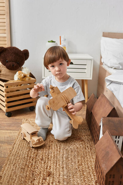 vertical shot of adorable little boy playing actively with wooden plane and looking at camera