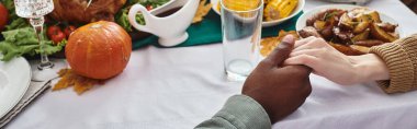 banner of multiethnic man and woman holding hands, praying on Thanksgiving next to festive dinner clipart
