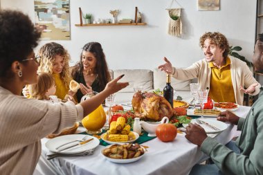 happy multiracial family having active conversation and gesturing at Thanksgiving table with turkey clipart