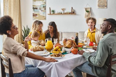 Mutlu çok ırklı aile ve arkadaşlar Şükran Günü yemeğinde konuşuyor ve gülümsüyor.
