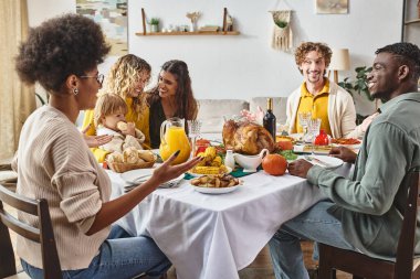 Mutlu ırklar arası aile ve arkadaşlar Şükran Günü yemeğinde konuşuyor ve gülümsüyor.