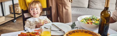banner of toddler girl looking away and smiling near pumpkin pie during Thanksgiving celebration clipart