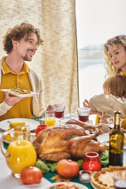 happy parents celebrating Thanksgiving with toddler daughter, curly man and woman having dinner clipart
