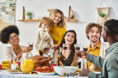 Mutlu Şükran Günleri, neşeli çoklu etnik arkadaşlar ve kırmızı şarap kadehleriyle tezahürat yapan aile üyeleri.