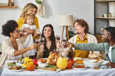 Mutlu Şükran Günleri, neşeli çoklu etnik arkadaşlar ve hindinin yanında kadeh tokuşturan şarap kadehleri.