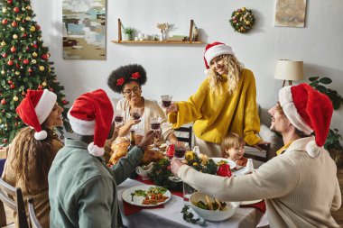 Noel Baba şapkalı mutlu çok ırklı arkadaşlar ve aileler Noel 'i kutlarken kadeh tokuşturuyor.