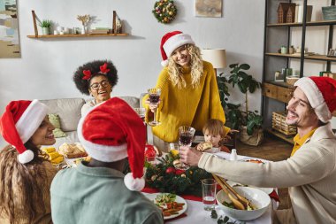 Merry Christmas celebration, happy multicultural friends and family cheering glasses near dinner clipart