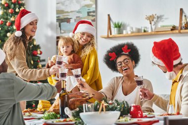 Noel Baba şapkası takıp şenlik masasında kadehlerini tokuşturan çok ırklı neşeli bir aile.