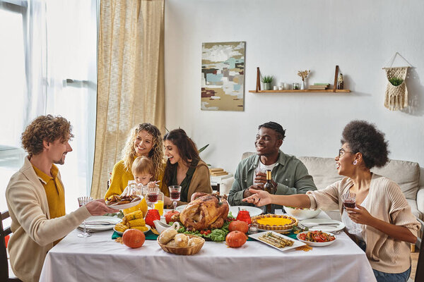 man passing plate with roasted potatoes to happy african american woman during Thanksgiving dinner