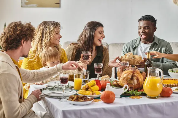 joyous interracial family and friends gathering at Thanksgiving table with various meals and drinks