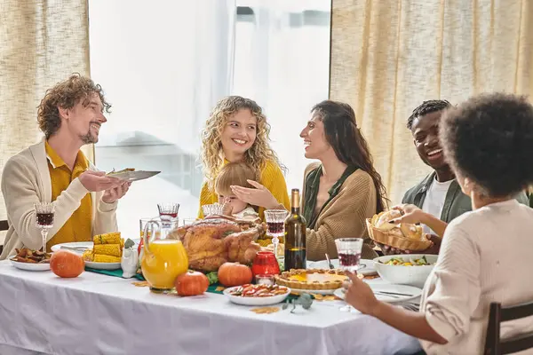 happy multiracial family and friends enjoying meals and drinks while gathering on Thanksgiving day