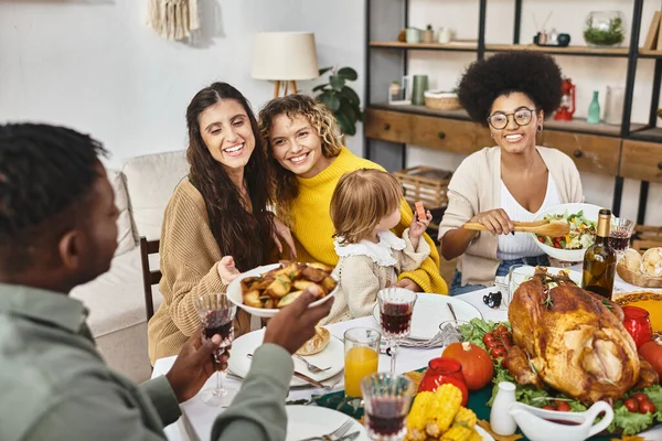 happy multicultural friends and lgbt family sharing meal while celebrating Thanksgiving together
