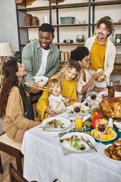 Happy Thanksgiving, cheerful multiethnic friends and family gathering at festive table with turkey