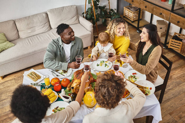 Thanksgiving, smiling multiethnic friends and family cheering glasses of wine near turkey, top view