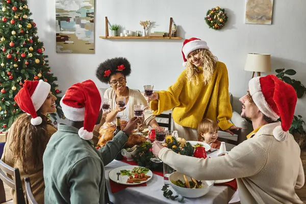 Happy multiethnic friends and family in santa hats clinking glasses while celebrating Christmas