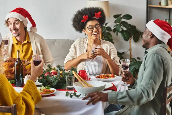 big multicultural family talking and smiling cheerfully at Christmas table wearing Santa hats