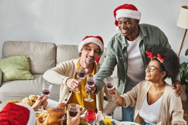 Çok ırklı büyük bir aile Noel 'de Noel sofrasında oturmuş şarap bardaklarını tokuşturuyor.