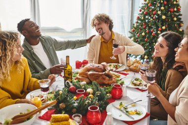 Çok ırklı, neşeli bir aile, arka planda Noel ağacı olan neşeli öğle yemeğine gülüyor ve gülümsüyor.