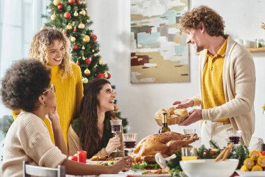 Genç ve neşeli bir adam elinde ekmek tabağı tutuyordu. Etrafı etnik çeşitlilikteki ailesiyle çevriliydi. Noel ağacı.