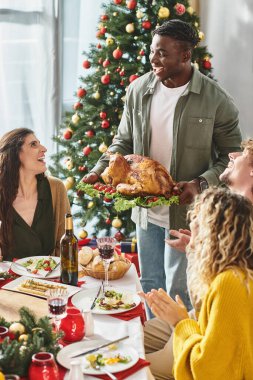 Büyük çok kültürlü bir aile Noel ziyafetinin tadını çıkarıyor. Şarap, hindi ve içtenlikle gülümsüyor.