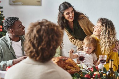 Mutlu çok ırklı aile üyeleri ellerinde kızlarıyla şenlik masasında oturmuş harika vakit geçiriyorlar.