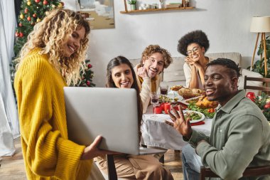 Çok ırklı bir aile Noel 'i öğle yemeğinde kutluyor, alkışlıyor ve dizüstü bilgisayar kamerasına samimi bir şekilde gülümsüyor.