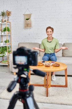 Bulanık dijital kamera ve bitki temelli diyet video bloğu yakınlarında vejetaryen ürünler sunan mutlu kadın.