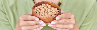 cropped view of woman holding wooden bowl with chickpeas, high-calorie plant-based food, banner clipart