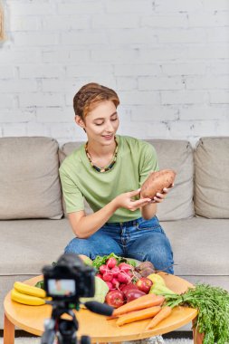 Taze sebzelerin yanında tatlı patatesli gülen kadın ve bulanık dijital kameranın önünde meyveler.