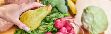 hand of vegetarian woman with delicious pier above blurred vegetables and fruits, horizontal banner clipart