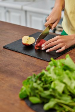 cropped view of woman cutting apple near fresh lettuce on worktop in kitchen, plant-focused diet clipart