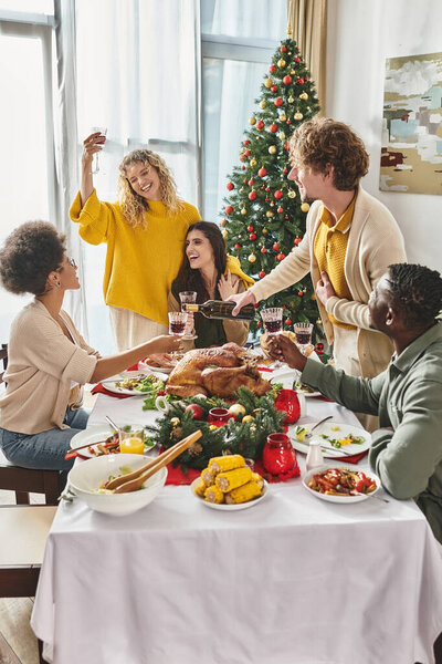 big multiethnic family gathered at festive table enjoying each other and drinking wine, Christmas