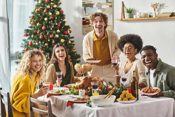 happy multicultural family laughing and smiling at camera with Christmas tree on background