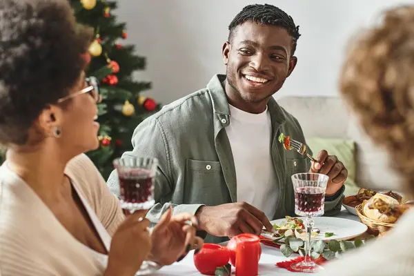 Mutlu Afro-Amerikan erkek ve kadın Noel masasında oturmuş, yemeklerini yiyor, birbirlerine gülümsüyorlar.