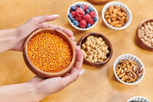 cropped woman with bowl of lentils near various berries and nuts on table at home, plants-based diet